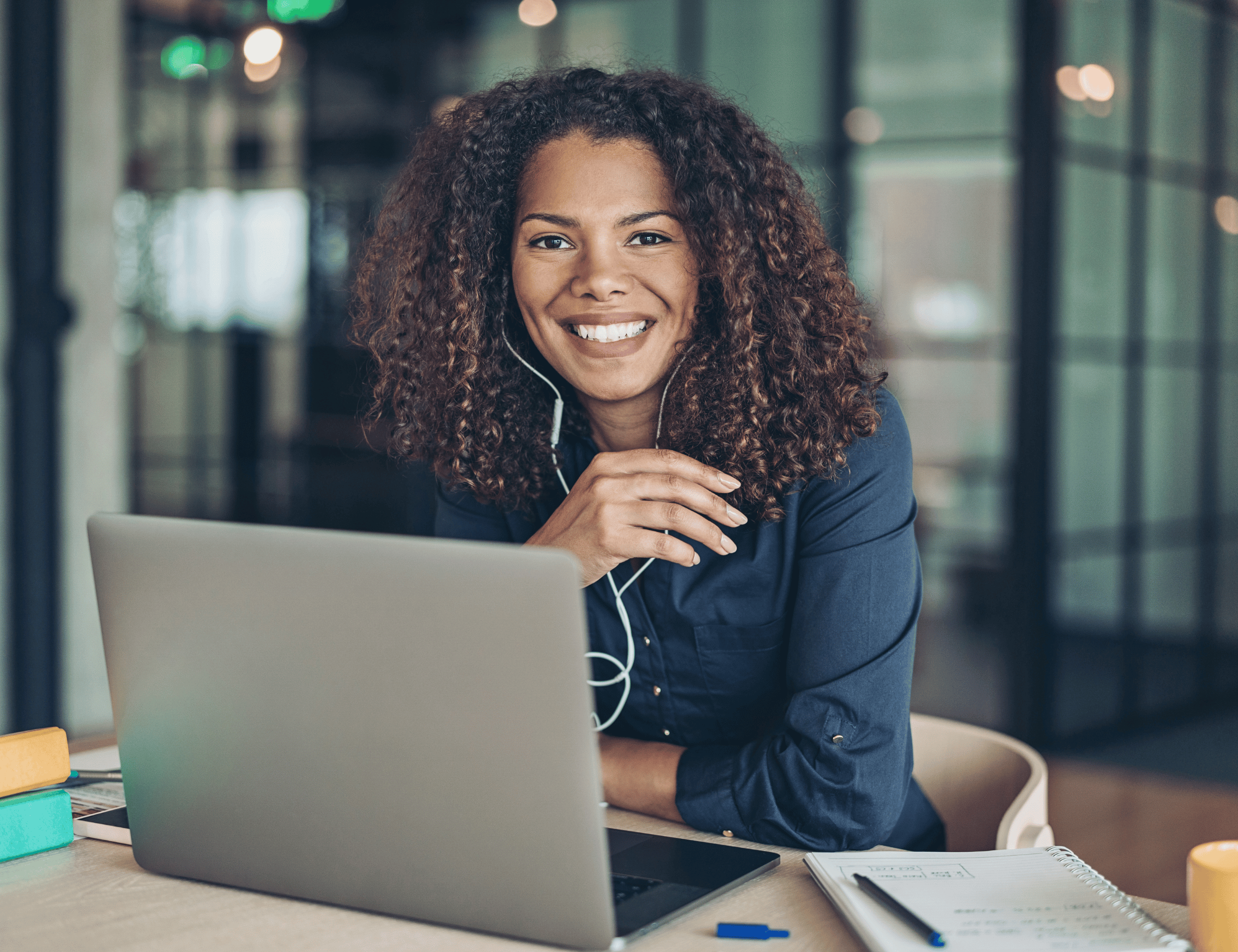 Femme souriante avec des écouteurs, travaillant sur son ordinateur portable dans un espace de coworking moderne